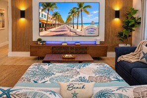 A living room with a large flat-screen TV displaying a beach scene, a wooden entertainment unit with books and a lamp, a blue sofa with a beach-themed throw, and a coffee table with a tray. - Premium Oversized Vacation Condo! Steps to the Broadwalk & Beach.
Game Lounge. (Hollywood)