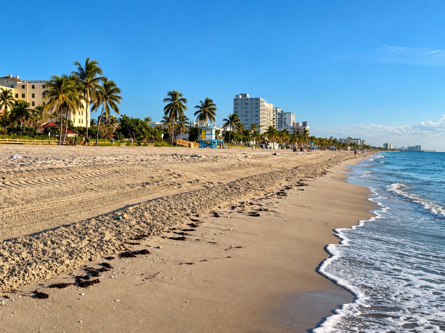 A beach with a sandy shore, palm trees, and buildings in the background.
