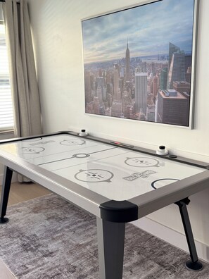A room with a glass-top table, a cityscape painting on the wall, and a window with curtains. - Premium Oversized Vacation Condo! Steps to the Broadwalk & Beach.
Game Lounge. (Hollywood)