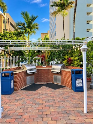 Un espace barbecue extérieur équipé de deux grils, entouré d’un mur de briques et d’une clôture blanche.