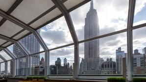 Un interior moderno con ventanas amplias que ofrecen vistas de un horizonte urbano, incluyendo un rascacielos destacado.
