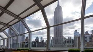 A modern interior with large windows offering views of a city skyline, including a prominent skyscraper. - NYC Stay Near Times Square, Broadway & Dining with King Guest Room Comfort (New York)
