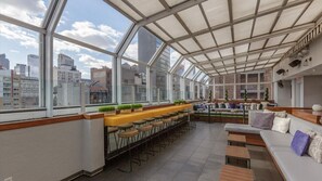 A modern rooftop bar with a glass ceiling, seating areas, and a city view.