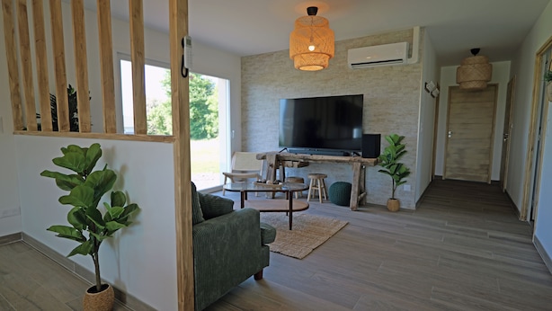 A modern living room with a flat-screen TV, wooden furniture, and a large window. - Evasion Campagne : Spa, Sauna, Sport (ST MARDS DE BLACARVILLE)
