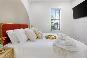 A bedroom with a bed, a window, and a flat-screen TV on the wall. - Boston Charm 2BR2BTH / 8 Minutes to Boston (Somerville)