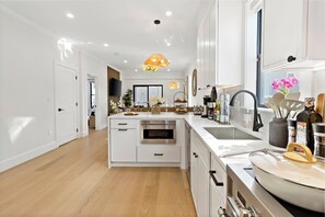 Una cocina moderna con armarios blancos, horno empotrado, una isla grande con lavamanos e iluminación colgante.