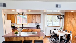 A modern kitchen with wooden cabinets, a central island with stools, and a dining area with a table and chairs.
