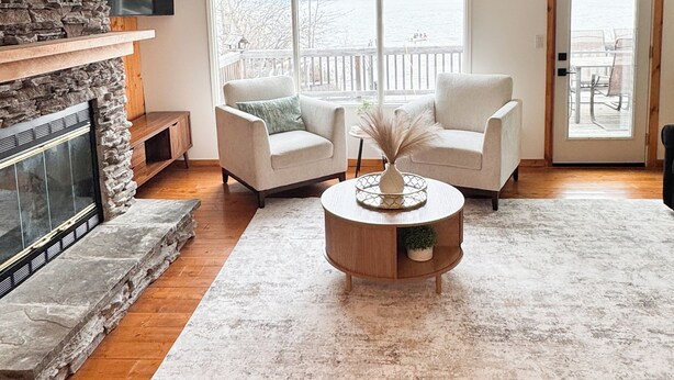 A living room with a fireplace, two armchairs, a coffee table, and a view of the water.