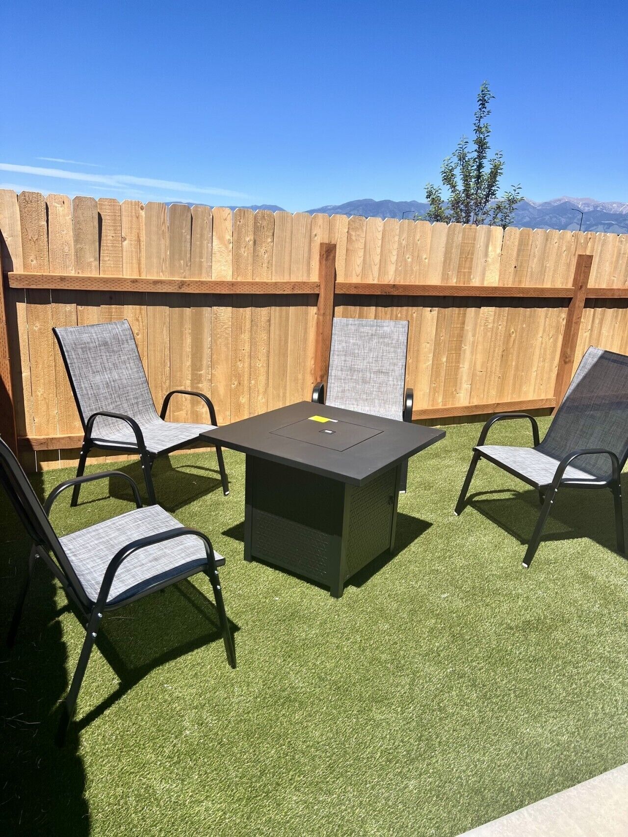 Eine Terrasse im Freien mit einem Tisch und vier Stühlen, umgeben von einem Holzzaun und Blick auf Berge.