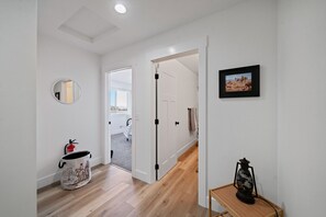 A hallway with a wooden floor, a round mirror, a fire extinguisher, a small table with a lantern, and a door leading to another room. - The Guss Stop l Gallatin House (Belgrade)