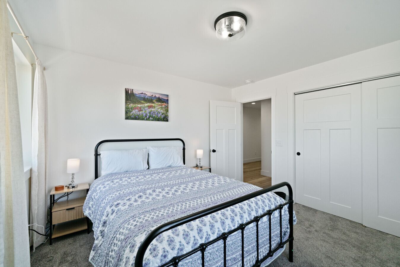 A bedroom with a bed, bedside tables, a painting, and a ceiling light fixture.