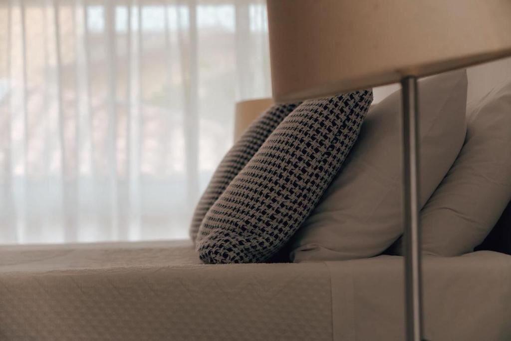 A bed with a patterned pillow and a plain pillow, a metal headboard, and a window with blinds.