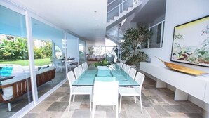 Un espace de salle à manger moderne avec une table et des chaises en verre, un escalier et une vue sur un jardin.