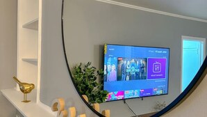 Un téléviseur fixé au mur, avec un miroir rond au-dessus, une petite plante et un panneau décoratif.