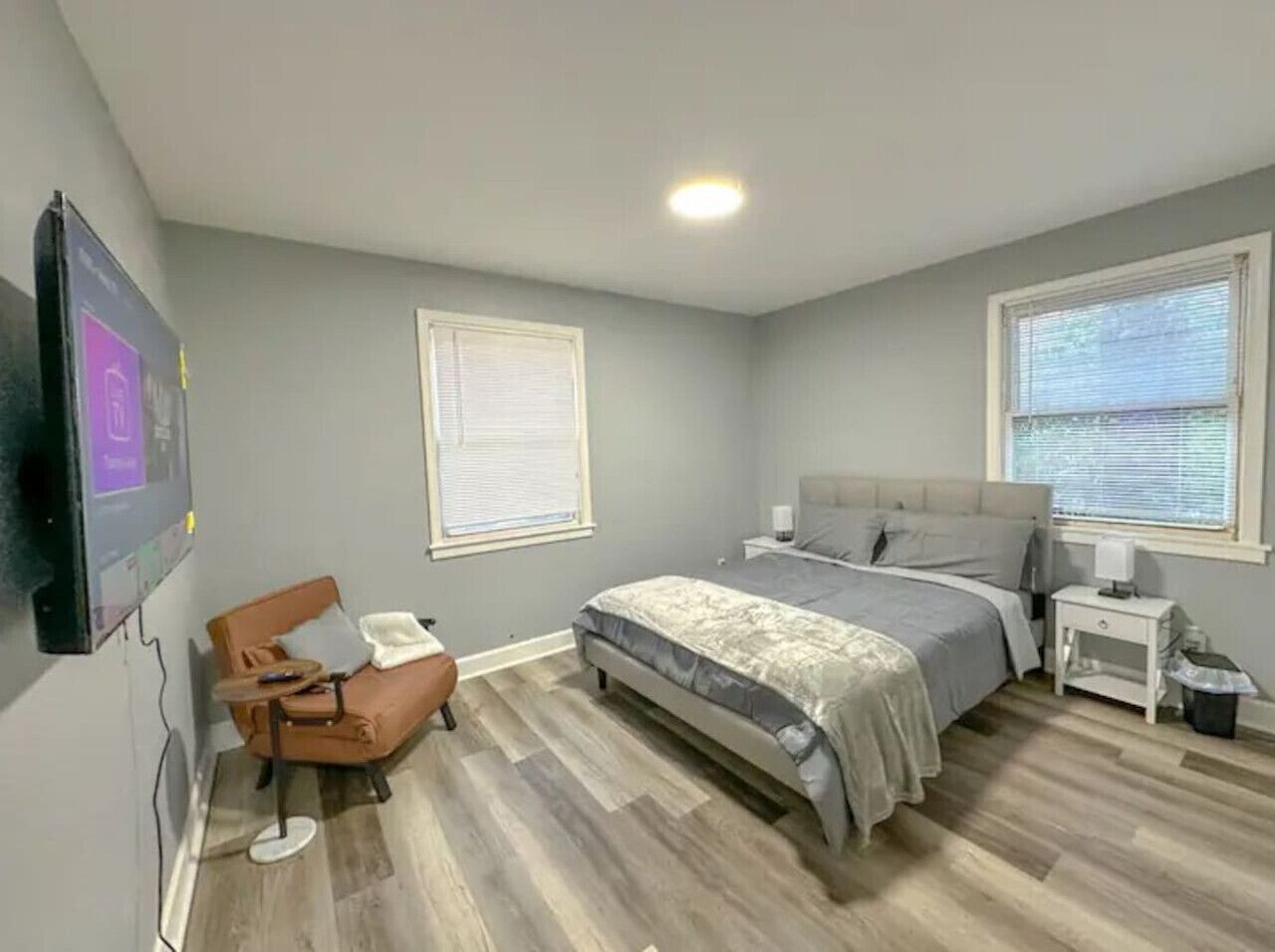 Un dormitorio con cama, una silla, un televisor y una ventana.