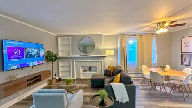 Un salon moderne doté d’un téléviseur à écran plat, d’une cheminée, d’un coin repas avec une table et des chaises, et d’un ventilateur de plafond.