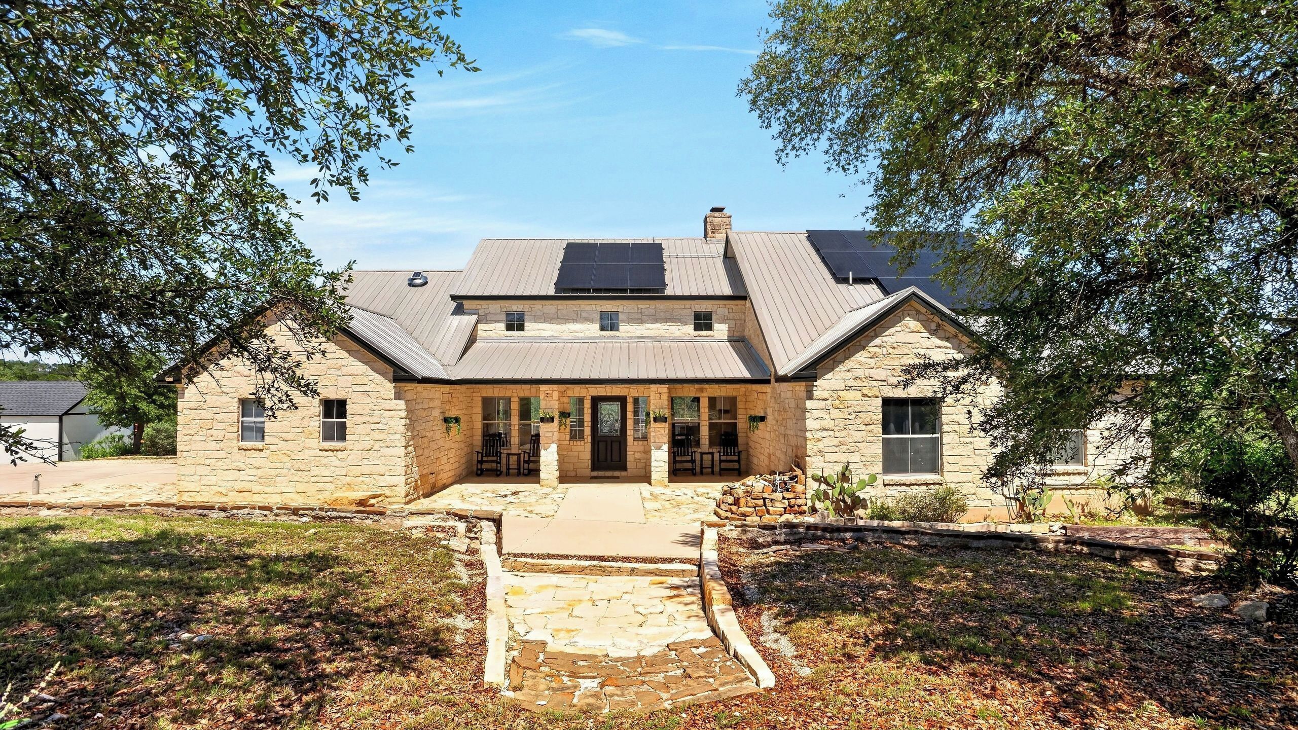 A stone house with a central entrance, solar panels, and a stone pathway leading to the door.
