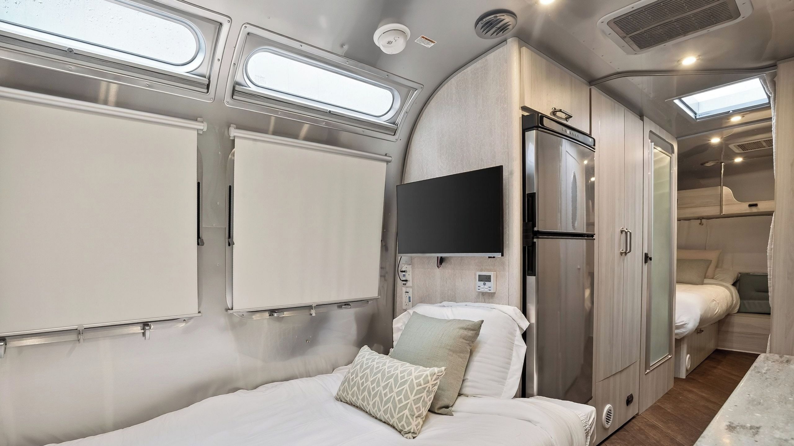 Interior compacto de una autocaravana con cama, refrigerador, televisor y ventana.