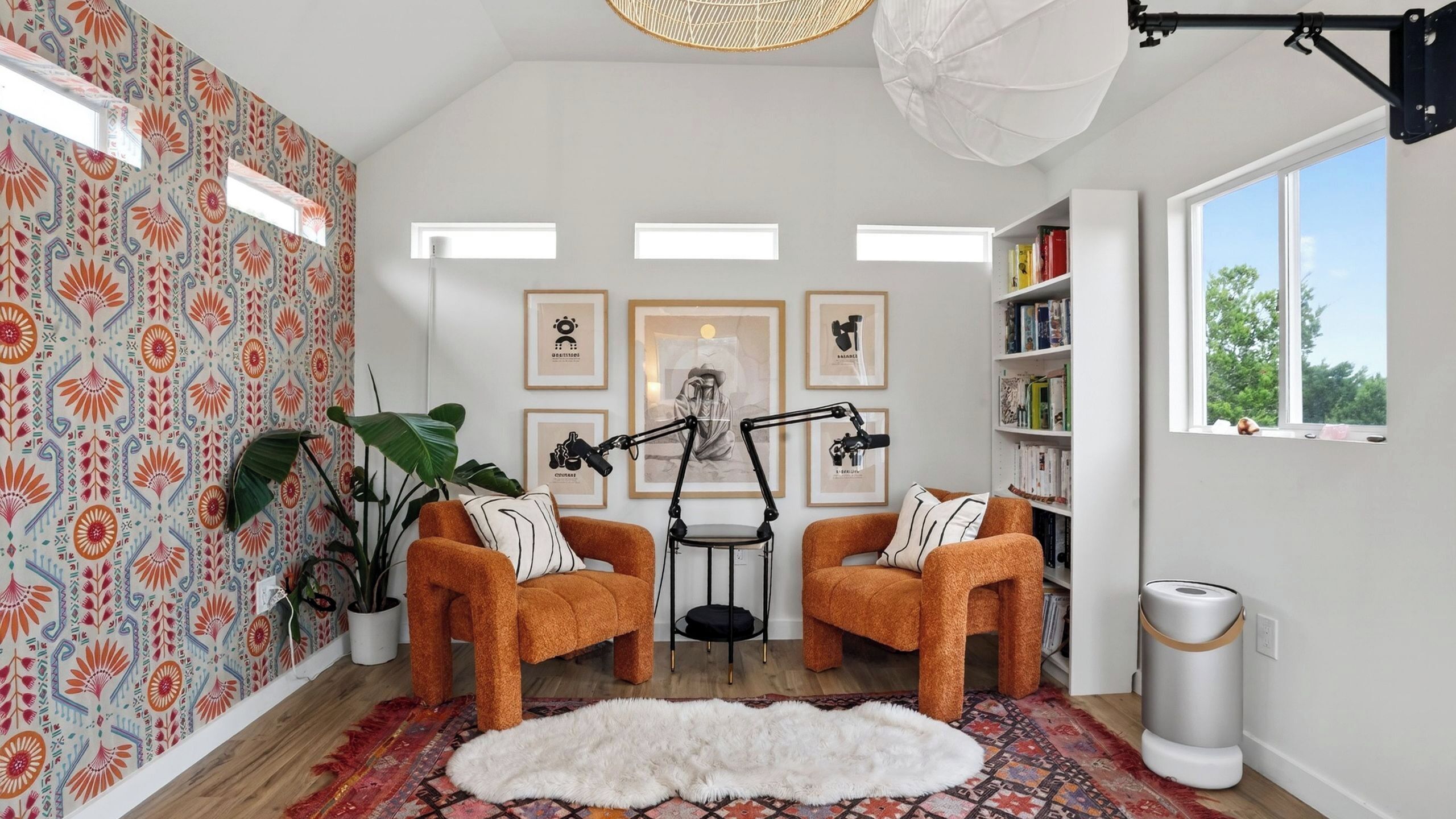 A cozy room with two orange armchairs, a white furry rug, a standing lamp, and a bookshelf.