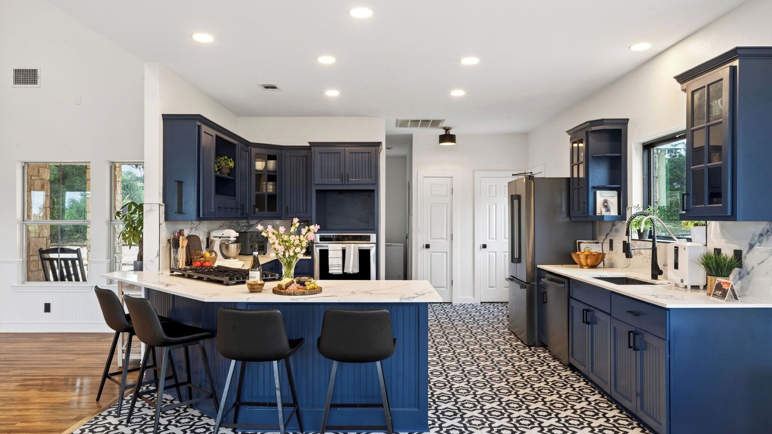 A modern kitchen with dark blue cabinets, a central island with bar stools, a stainless steel refrigerator, and a patterned floor.