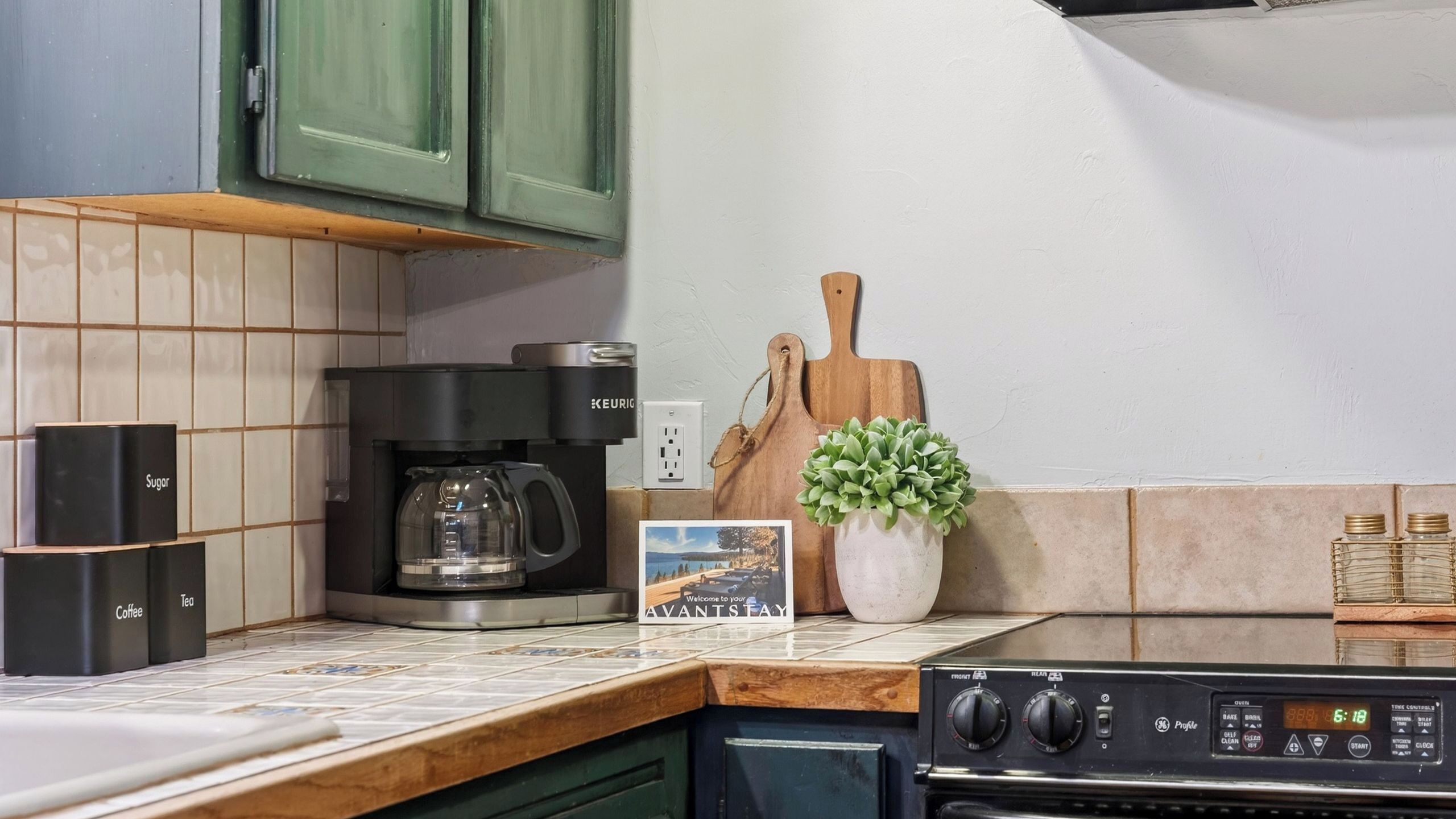 A kitchen with a coffee maker, sugar and tea containers, a small potted plant, and a stove.