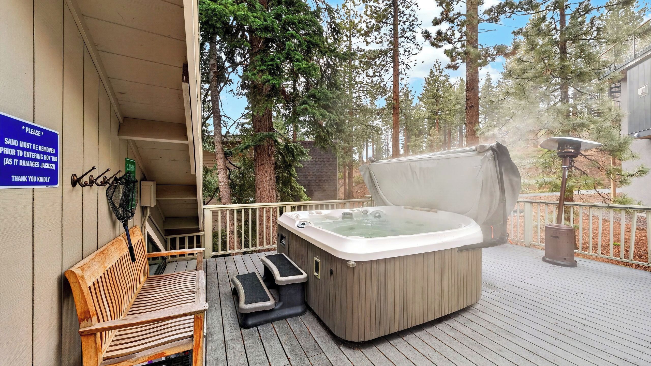 A hot tub on a wooden deck with a bench and a sign about sand removal.