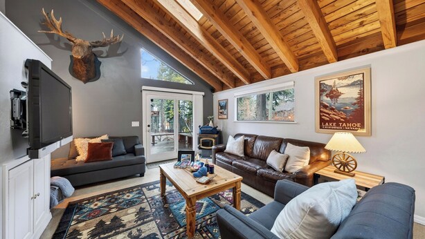 A cozy living room with a fireplace, leather sofas, a mounted deer head, and a poster of Lake Tahoe. - Incline Pines Retreat by Avantstay Private Hot Tub + Wraparound Deck + Views Near Dining and Shops (Incline Village)
