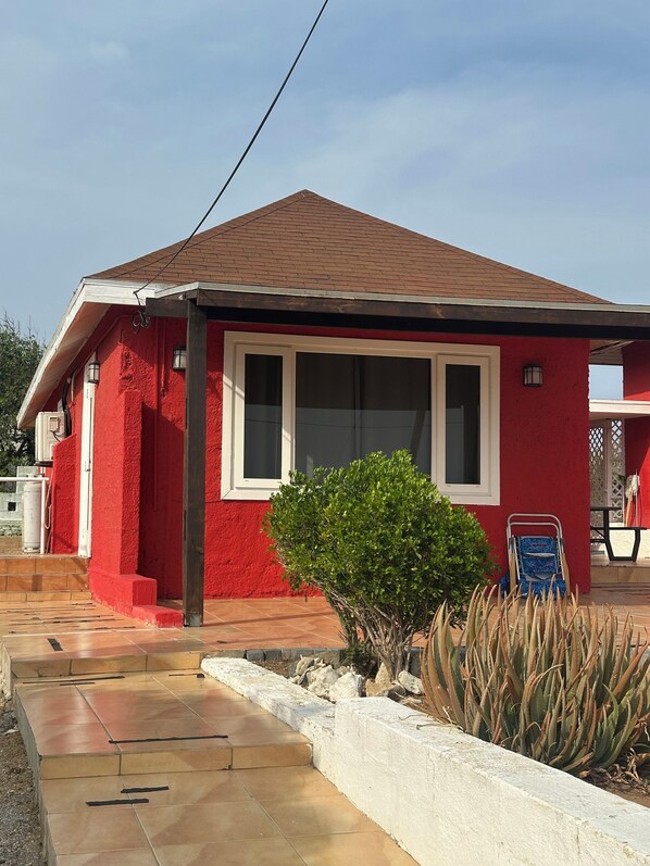 A red building with a tiled roof, a small garden with plants, and a blue chair.