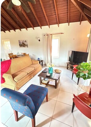 A living room with a sofa, a coffee table, a television, and a chair. - Located in Baby Beach • Cute 2BR/1BA Casita • Walk to Baby & Rodgers Beach (San Nicolas)