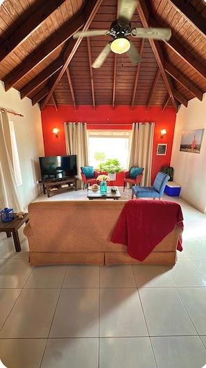 Una sala de estar acogedora con televisor, dos sillones, un sofá y un ventilador de techo.