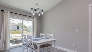 A dining area with a white table and chairs, a chandelier, and a view through a large window. - ‼️Citrus Springs 3BR - Gulf & Springs 30 Min (Citrus Springs)