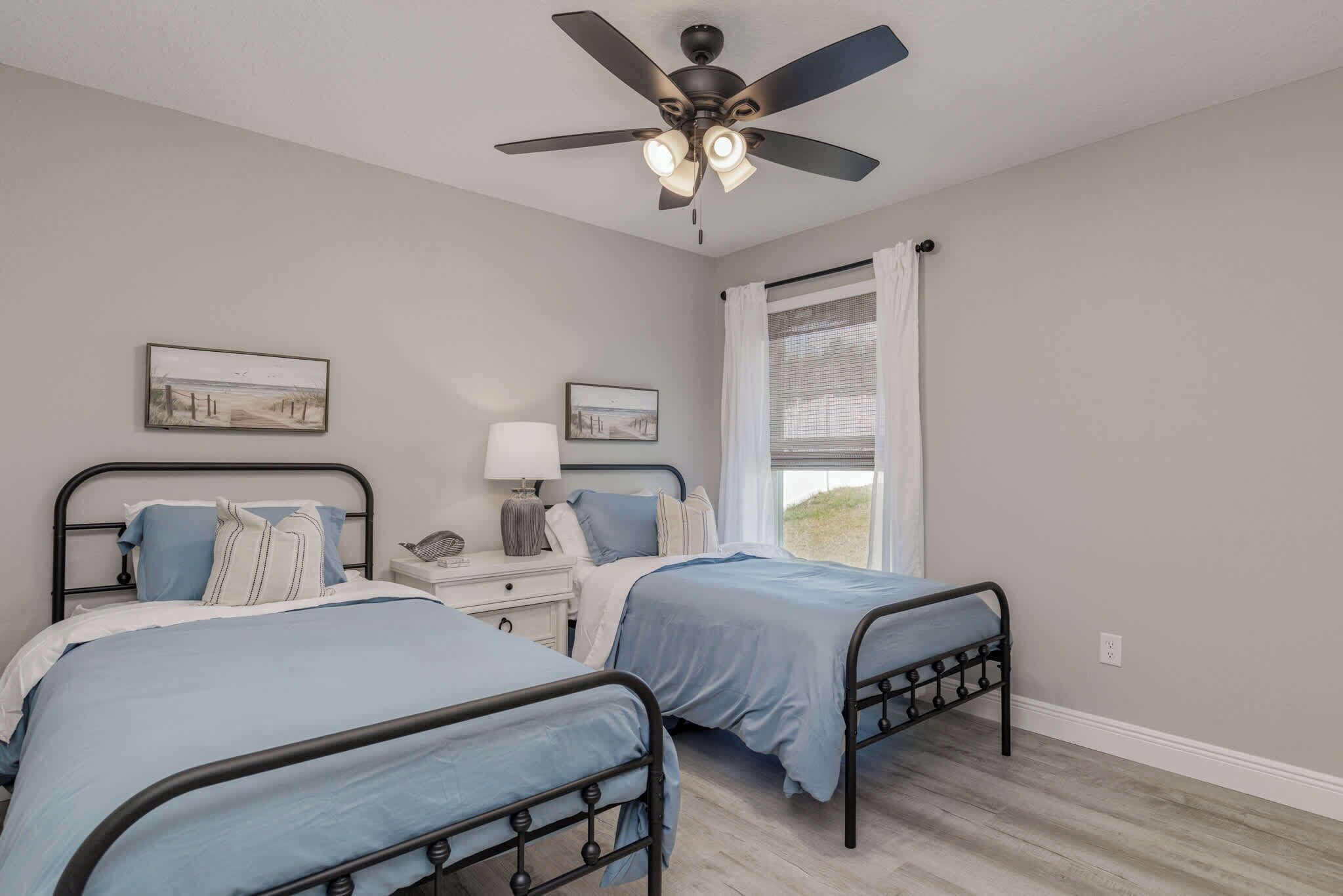 A bedroom with two beds, a ceiling fan, a nightstand, and a window with curtains.