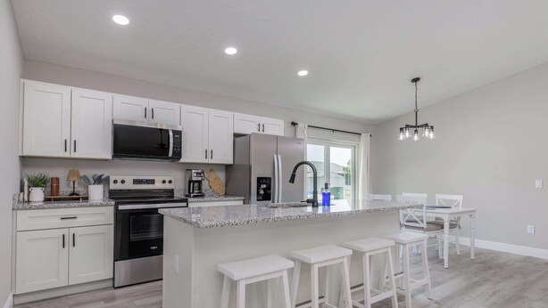 A modern kitchen with white cabinetry, stainless steel appliances, a central island with bar stools, and a chandelier. -   ‼️Citrus Springs 3BR - Gulf & Springs 30 Min (Citrus Springs)