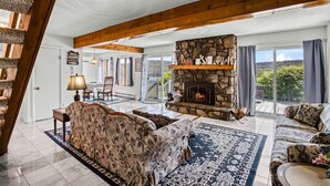 A spacious living room with a stone fireplace, wooden beams, and a view of the outdoors. - Terra Alta Lake View - Pool, Game Room (Terra Alta)