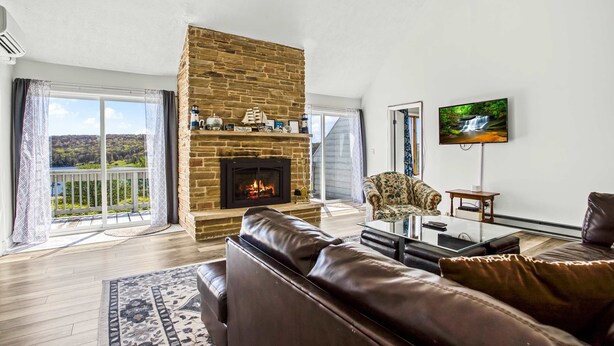 A living room with a fireplace, leather sofa, television, and a balcony with a view of greenery. - Terra Alta Lake View - Pool, Game Room (Terra Alta)