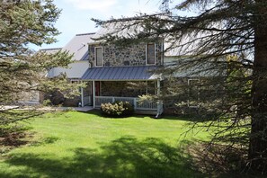 A stone house with a metal roof, a covered porch, and a well-maintained lawn. - Terra Alta Lake View | Nearby Resort Pool & Games (Terra Alta)