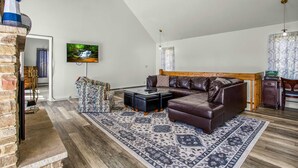 A spacious living room with a brown leather sofa, patterned rug, and a television on the wall. - Terra Alta Lake View - Pool, Game Room (Terra Alta)