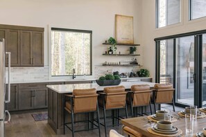 A modern kitchen with a large island, bar stools, and a dining table set for six. - The Canopy House - Hot Tub, Sauna, Mountain View (Blue Ridge)