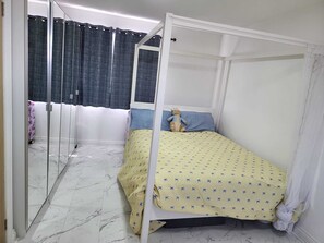 A bedroom with a four-poster bed, a mirror, a window with curtains, and a patterned bedspread.
