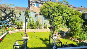 Un jardín con muro de ladrillo, un arco de metal y diversas plantas.