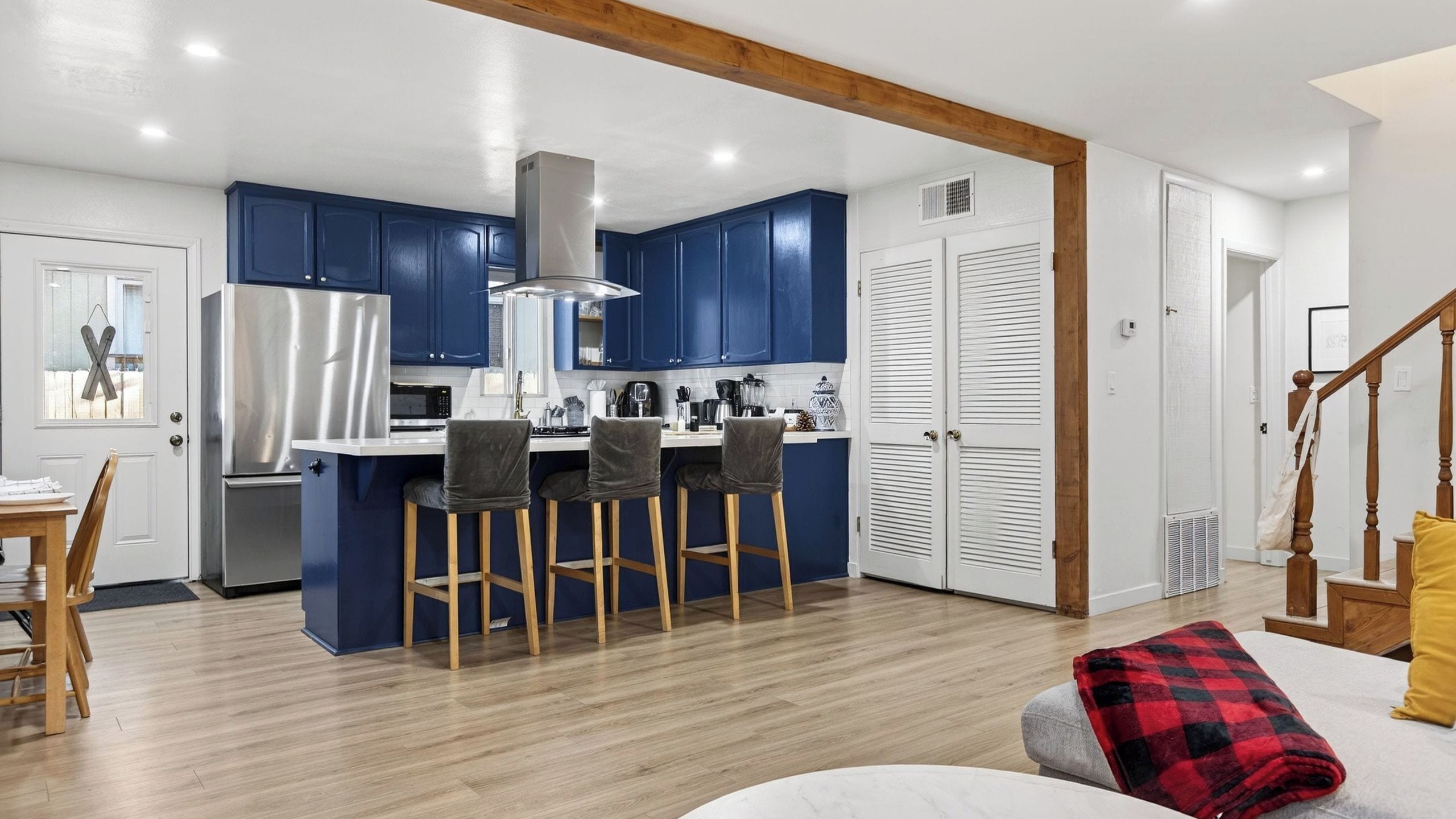 A modern kitchen with blue cabinets, a stainless steel refrigerator, and a bar area with stools.