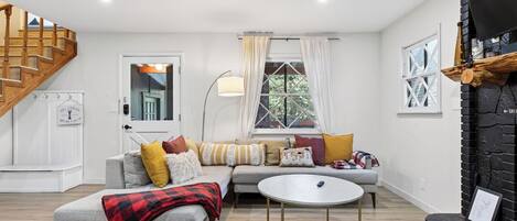 Una sala de estar con sofá, mesa de centro, chimenea y escalera.