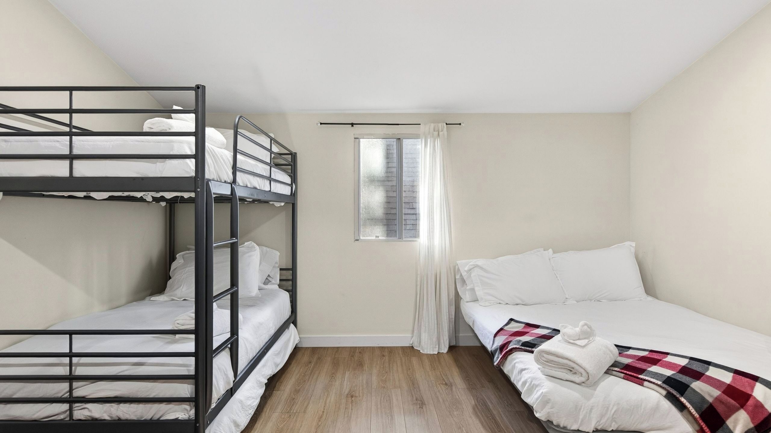 Une chambre avec des lits superposés, une fenêtre avec des rideaux et une couverture à carreaux sur le lit du bas.