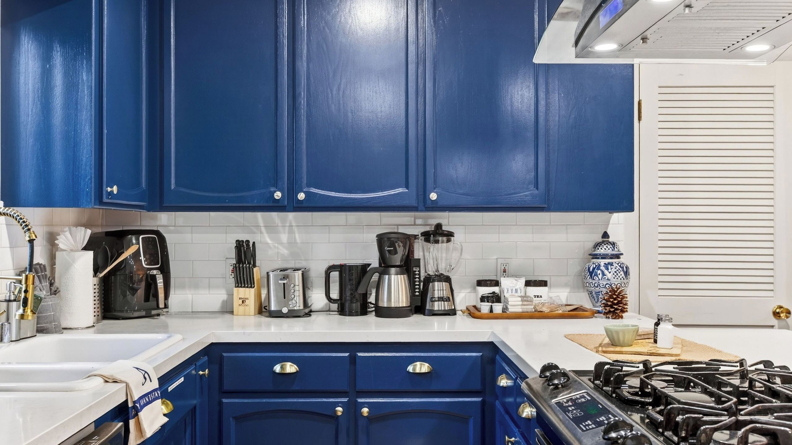 A kitchen with blue cabinets, a gas stove, a coffee maker, and various kitchen utensils.