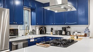 A modern kitchen with blue cabinets, a stainless steel refrigerator, a gas stove, a coffee maker, and a microwave.