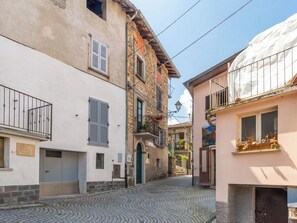Eine Kopfsteinpflasterstraße, gesäumt von historischen Gebäuden mit bepflanzten Balkonen, strahlend blauer Himmel und einer Mischung unterschiedlicher Architekturstile.