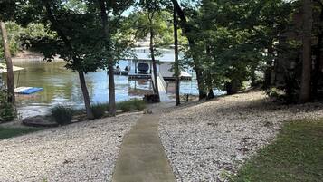 Un chemin en béton qui mène à un quai au bord d’un lac, entouré d’arbres et d’un bâtiment.