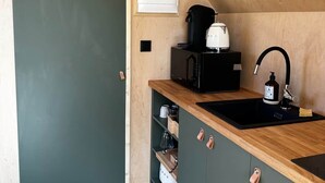 A small kitchenette with a black sink, a coffee maker, and a shelf with jars.