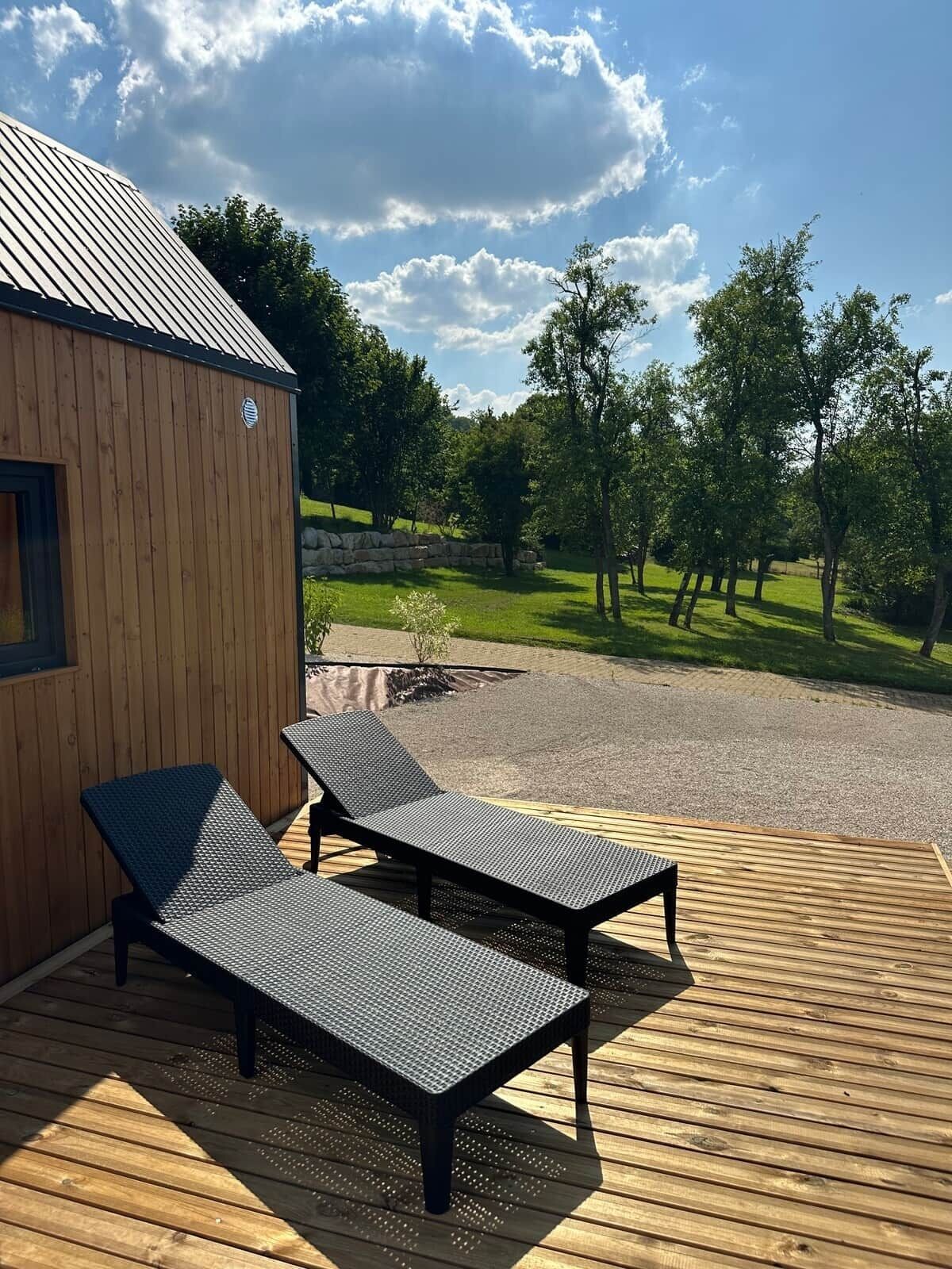 A wooden deck with two lounge chairs and a small building with a metal roof.