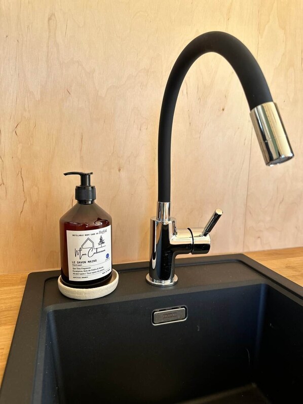 A black sink with a chrome faucet and a soap dispenser on the countertop.